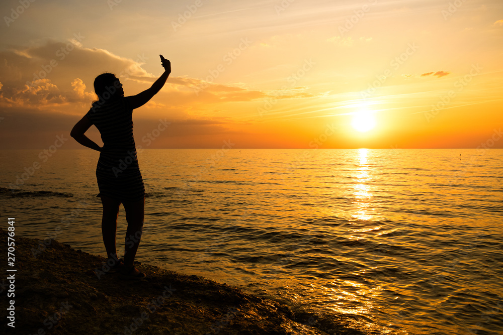 Fototapeta premium silhouette of a young girl. makes selfie at sea sunset.