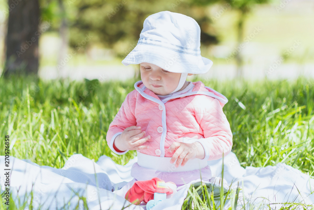 Child sitting on the blanket on the green grass, summer time, outdoors Child sitting on the blanket on the green grass, summer time, outdoors