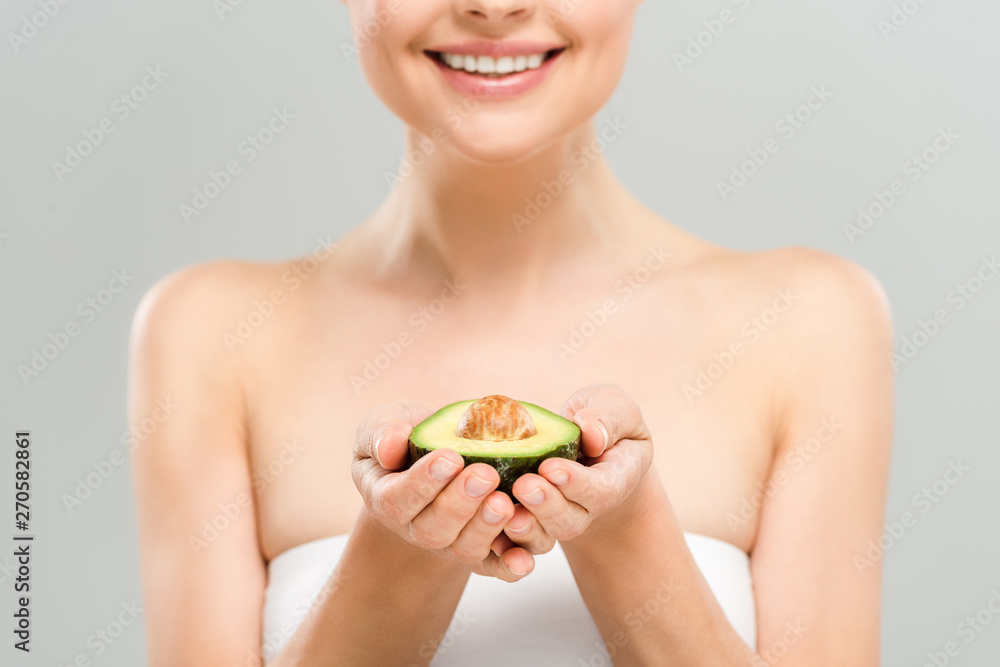 cropped view of cheerful woman holding half of ripe avocado isolated on grey cropped view of cheerful woman holding half of ripe avocado isolated on grey