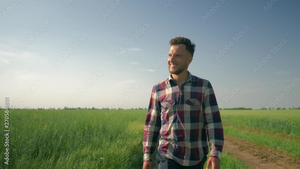 smiling male farmer enjoy the fresh air and the beauty of nature, young man goes to the camera on background of green field and blue sky smiling male farmer enjoy the fresh air and the beauty of nature, young man goes to the camera on background of green field and blue sky