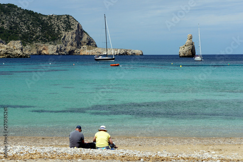 A pair of elderly people sitting by the sea.Benirras Bay.Ibiza Island.Spain. photo