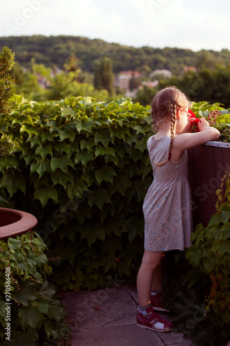 cute young girl in a beautiful dress playing with flowers on the balcony