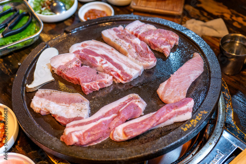 Pan-fried black pork meal in Korea restaurant, fresh delicious korean food cuisine on iron plate with lettuce, close up, copy space, lifestyle