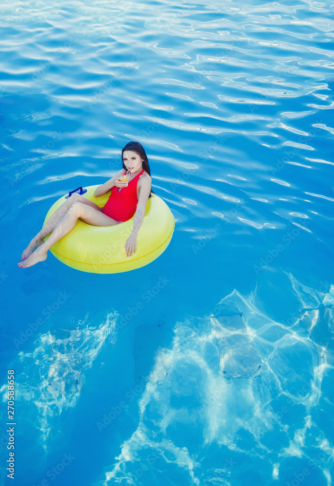 beautiful woman with juice in a red swimsuit lying on inflatable mattress in the pool