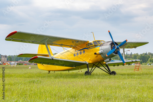 Yellow painted legendary soviet aircraft biplane Antonov AN-2 parked on a green grass of airfield against cloudy sky