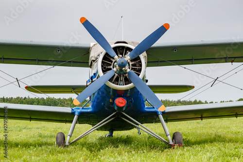 White and blue soviet aircraft biplane Antonov AN-2 parked on a green grass of airfield against cloudy sky