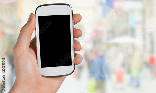 Hand holding smartphone on blurred city background, bokeh