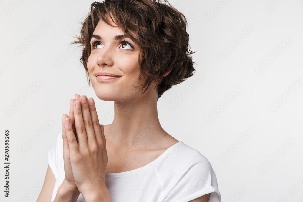 Portrait of confident woman with short brown hair in basic t-shirt keeping palms together and praying Portrait of confident woman with short brown hair in basic t-shirt keeping palms together and praying
