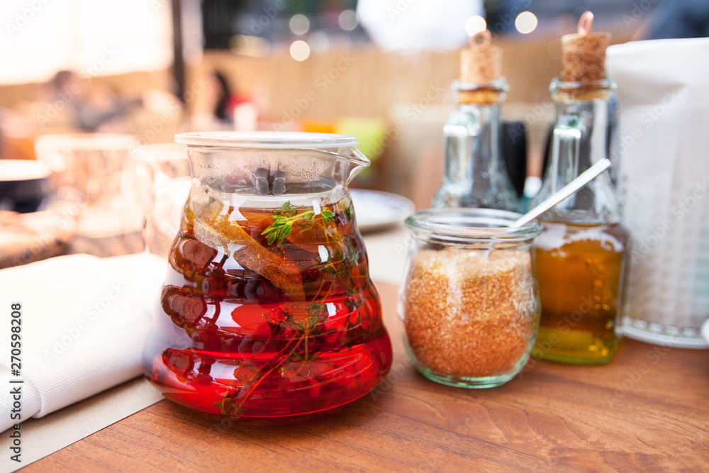 Glass teapot with fruit tea in a restaurant on wooden table. Glass jug with sangria in bar. Glass jug with organic fresh juice with fruit in cafe. Glass teapot with fruit tea in a restaurant on wooden table. Glass jug with sangria in bar. Glass jug with organic fresh juice with fruit in cafe.