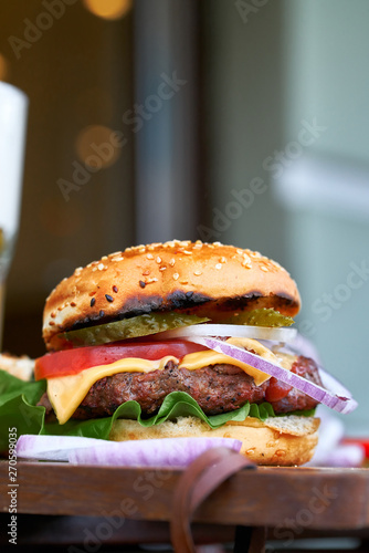Home made hamburger with beef, onion, tomato, lettuce and cheese. Fresh burger closeup on wooden rustic table with potato fries, beer and chips. Cheeseburger.