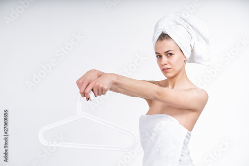 beautiful young nude girl in a towel holding a hanger for clothes. On an empty background.