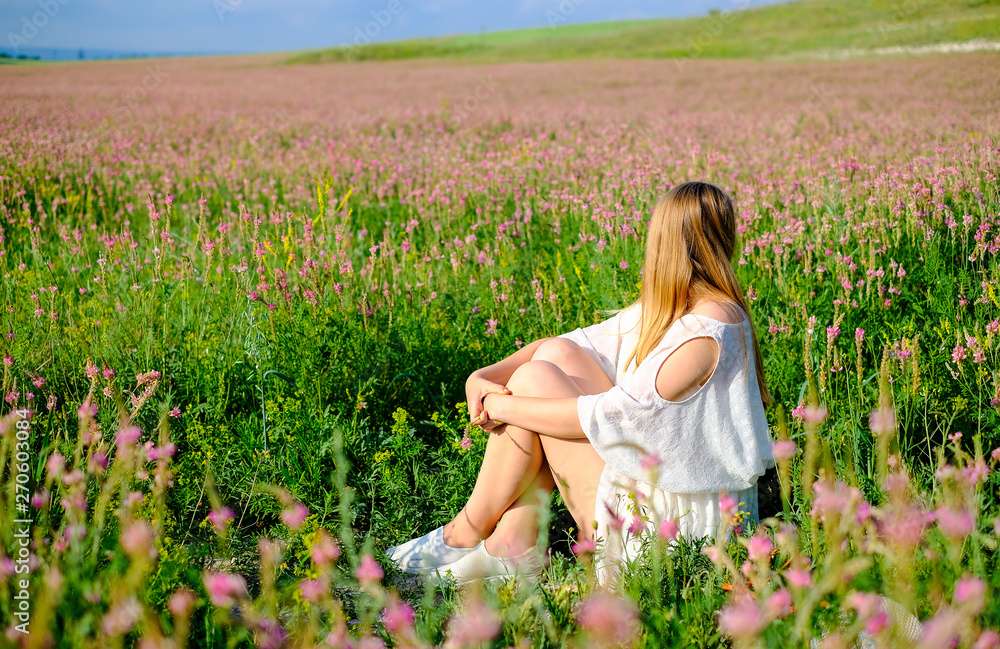 Girl sitting on flowered Sainfoin field. Girl on a blooming field of pink Girl sitting on flowered Sainfoin field. Girl on a blooming field of pink