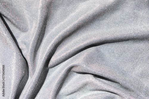 Background of light gray draped fabric with silver lurex thread. Beautiful fashionable fabric with a shiny thread for making clothes. Neutral background texture.