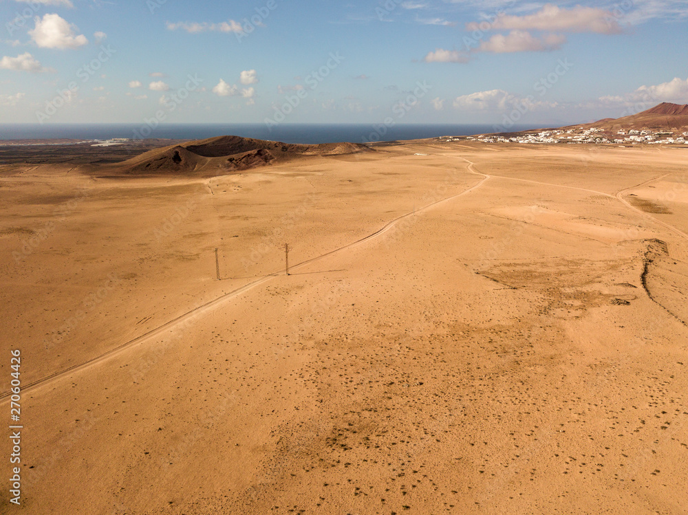 Aerial view of a desert landscape on the island of Lanzarote, Canary Islands, Spain. Road that crosses a desert. Reliefs on the horizon. Volcanoes. Aerial view of a desert landscape on the island of Lanzarote, Canary Islands, Spain. Road that crosses a desert. Reliefs on the horizon. Volcanoes.