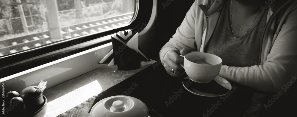 A young woman is sitting on a train with a cup of coffee and is looking out