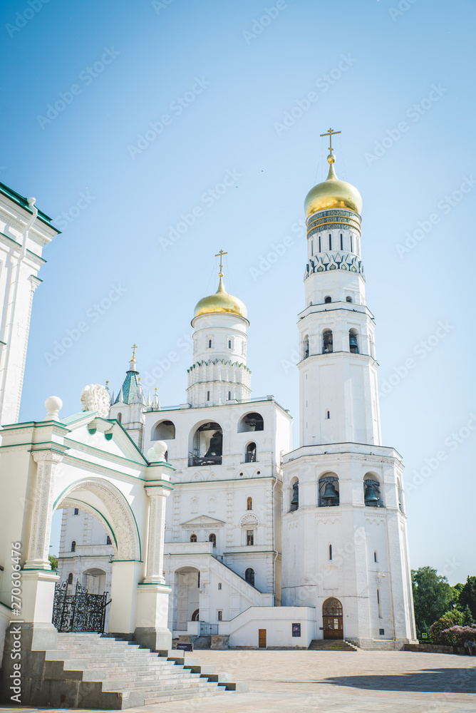 Fototapeta premium Tilt down on Ivan the Great Bell Tower cathedral inside Moscow Kremlin with clouds and blue sky in background