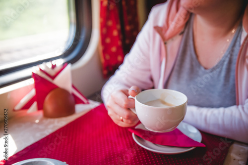 A young woman is sitting on a train with a cup of coffee and is looking out