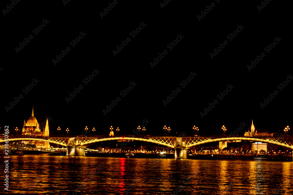 Fototapeta premium night Budapest, glowing in gold. The bridge over the Danube is illuminated by light bulbs. photo from the river