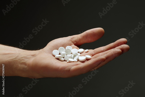 A handful of pills in the male hand on a dark background.