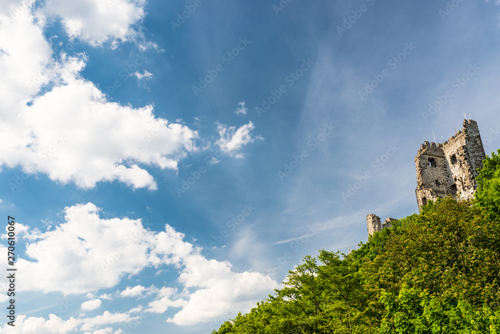 The ruins of a historical tower on a hill covered with trees in the background of blue sky with white clouds.