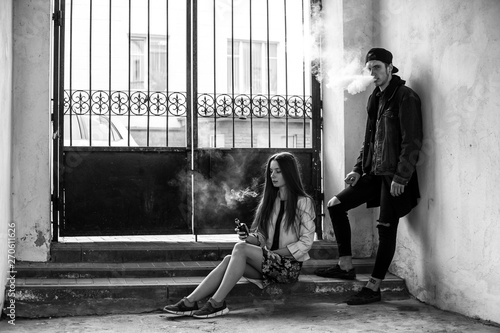 Vape teenager. Young cute girl in casual clothes and handsome guy in a cap smoke an electronic cigarette in prison cell. Bad habit that is harmful to health. Vaping activity. Black and white.