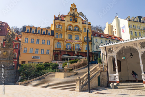 Outdoor sunny view of Holy trinity column, fountain and stairway beside Market colonnade, and background of Beautiful hotel's facade and colorful buildings in Karlovy Vary, Czech Republic.. 