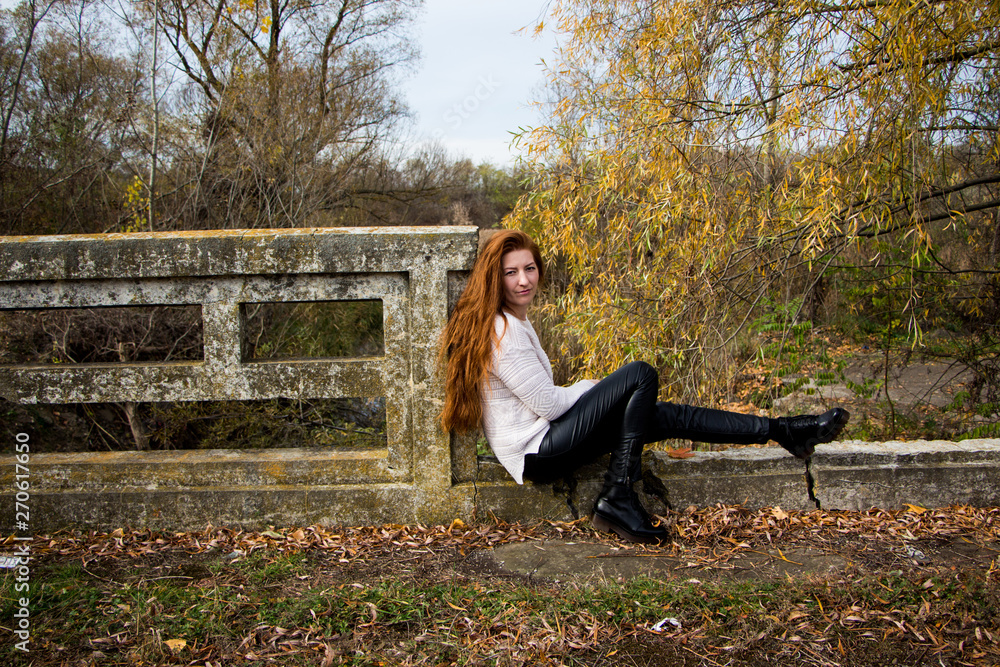 Portrait of young redhead woman sitting on a bench in autumn park Portrait of young redhead woman sitting on a bench in autumn park