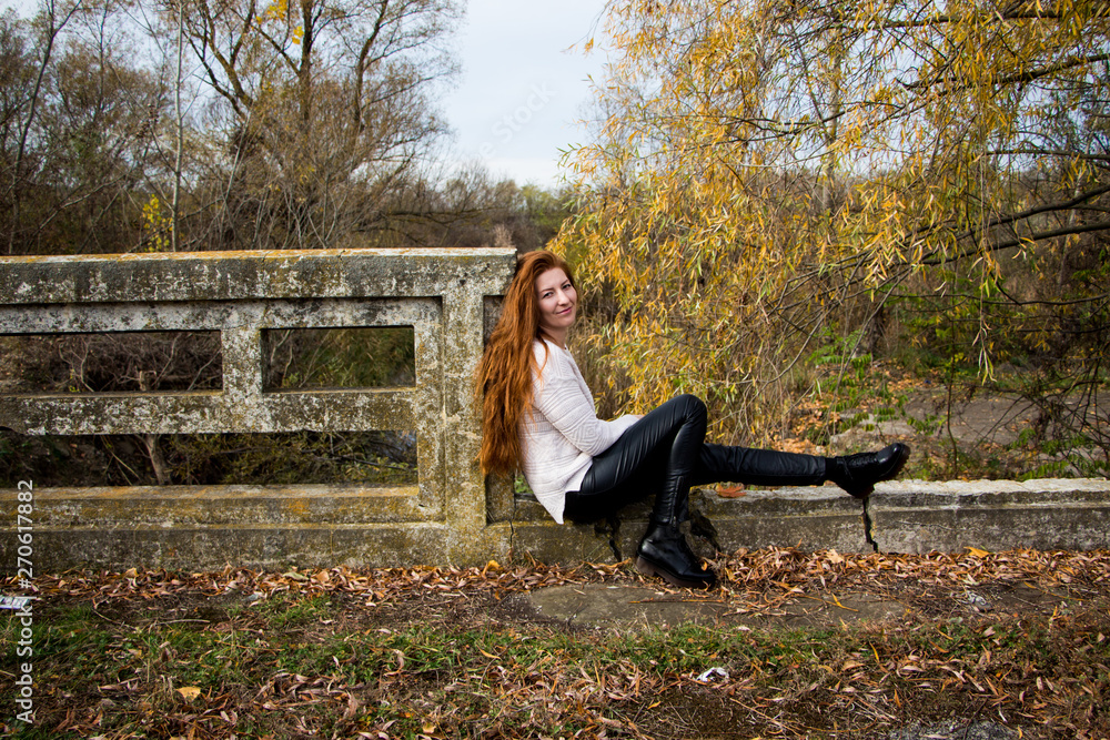 Portrait of young redhead woman sitting on a bench in autumn park Portrait of young redhead woman sitting on a bench in autumn park