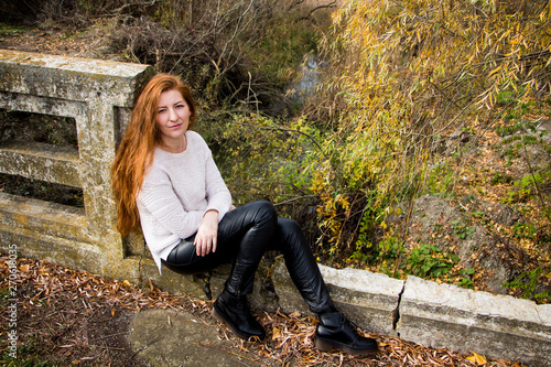 Portrait of young redhead woman sitting on a bench in autumn park photo