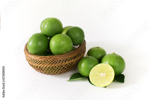 Lots of green lemon are in a wooden basket. And some of the outside with lemon slices cut in half on the side.