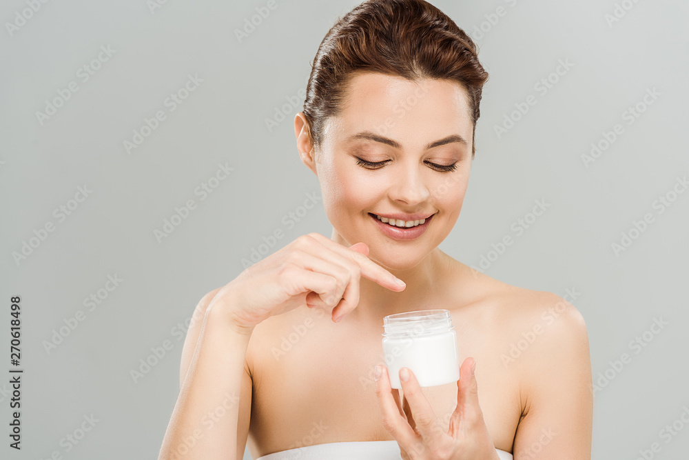 happy woman pointing with finger at container with face cream isolated on grey