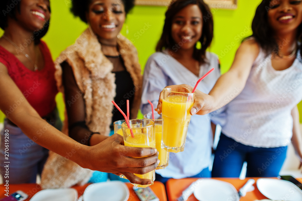Four young african girls in bright colored pizza restaurant clinking juices. Four young african girls in bright colored pizza restaurant clinking juices.