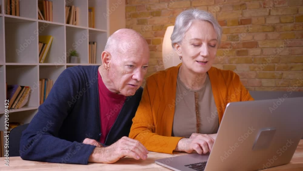 Two senior gray-haired caucasian colleagues working together with laptop being joyful in office. Two senior gray-haired caucasian colleagues working together with laptop being joyful in office.