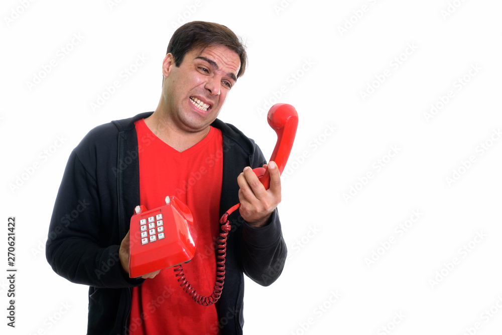 Studio shot of young angry Persian man holding and looking at ol Studio shot of young angry Persian man holding and looking at ol