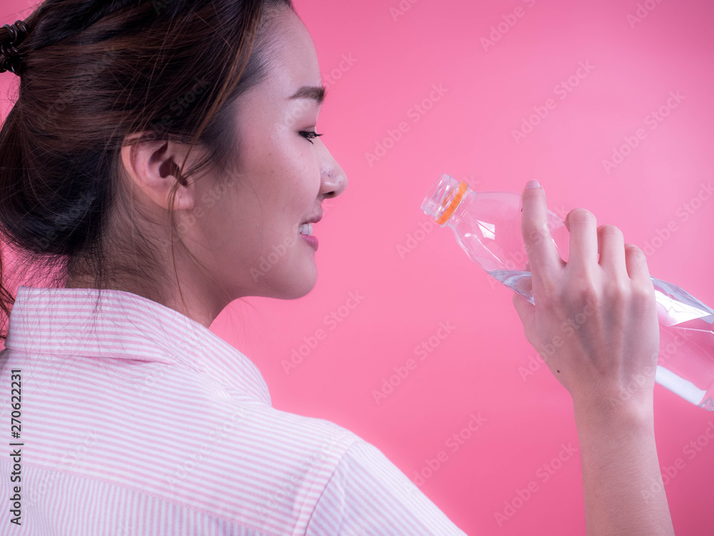 Beautiful asian young woman drinking a bottle of water isolated on a pink background. Beautiful asian young woman drinking a bottle of water isolated on a pink background.