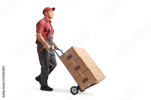 Obraz na plátně Young male worker in a uniform pushing boxes on a hand truck