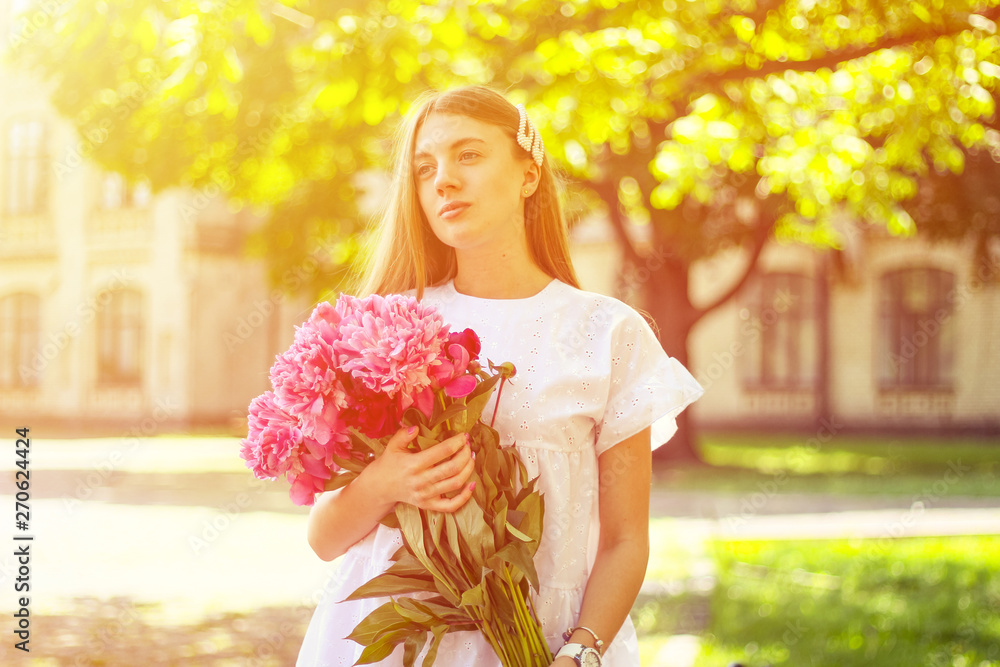 Fototapeta premium beautiful girl, no makeup, natural beauty, feminism. woman in a white dress, crosswise with a bouquet of peonies