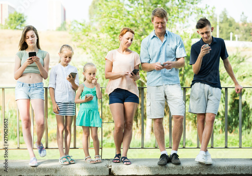Portrait of active large family standing with their mobile phones outdoors