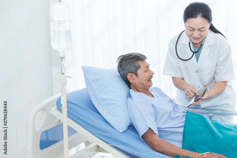 Female doctor discussing with happy senior patient over a report in tablet computer in the ward at hospital. Health and Happy concept.
