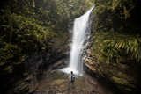 Young man from back looking at the waterfall in the middle of the jungle