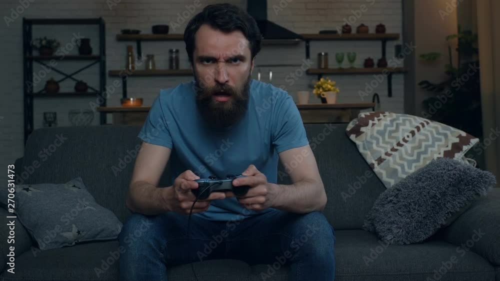 Beard man playing video games at home. Loosing game, beating joystick. Angry, disappointed, negative emotions. Beard man playing video games at home. Loosing game, beating joystick. Angry, disappointed, negative emotions.