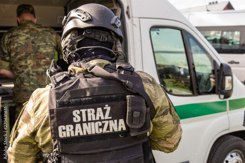 Polish Border Guard tactical unit officer in special uniforms, body armor with automatic weapons and communications equipment near a departmental vehicle. Inscription - Border Guard Polish Border Guard tactical unit officer in special uniforms, body armor with automatic weapons and communications equipment near a departmental vehicle. Inscription - Border Guard