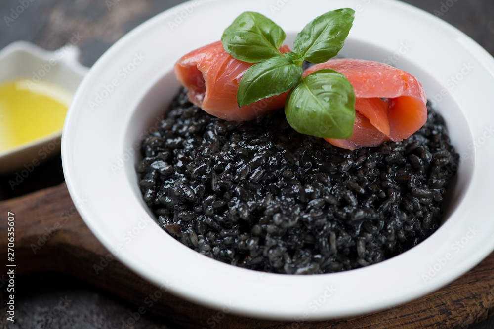 Squid-ink risotto with salmon fillet and fresh green basil in a white plate, closeup, selective focus Squid-ink risotto with salmon fillet and fresh green basil in a white plate, closeup, selective focus