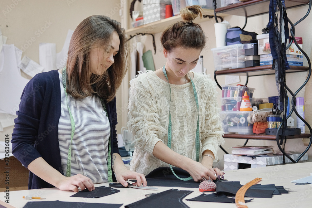 Fototapeta premium Seamstresses measure the fabric for sewing a dress in the atelier. Two female tailor working in in the sewing workshop.