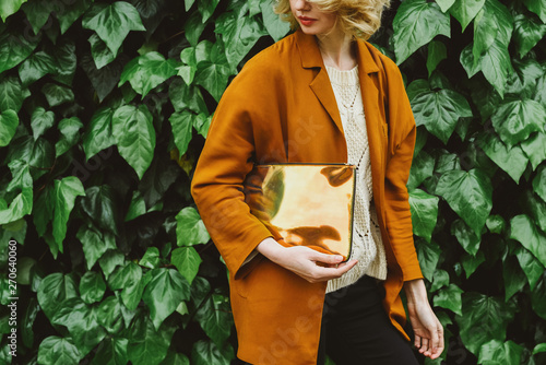 Woman with a clutch standing against ivy wall