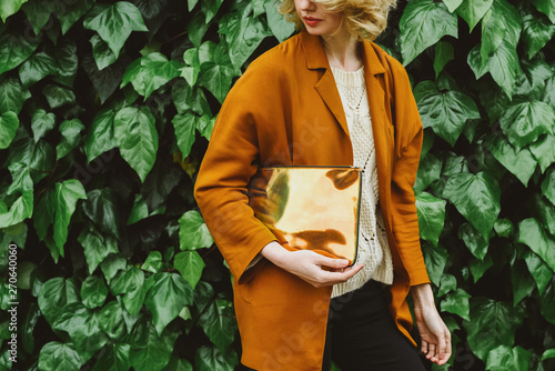 Woman with a clutch standing against ivy wall photo