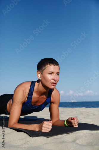 Woman doing plank exercise on beach in sunlight photo