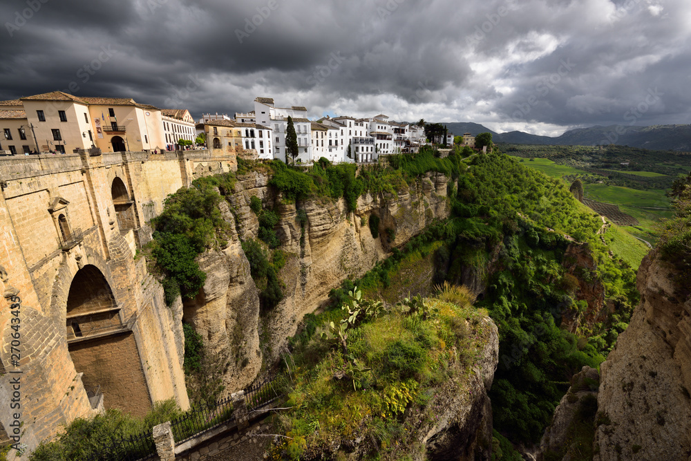 Dark clouds and dappled sunshine on cliff and new bridge of mountain city Ronda Spain