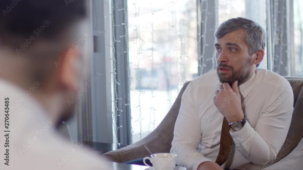 Rear view of two middle-aged Caucasian businessmen sitting during coffee break in café in front of each other and talkingRear view of two middle-aged Caucasian businessmen sitting during coffee break Rear view of two middle-aged Caucasian businessmen sitting during coffee break in café in front of each other and talkingRear view of two middle-aged Caucasian businessmen sitting during coffee break