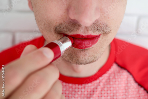 Close up of bearded man applying colorful red balm lipstick on his lips , on camera, lips, front view .